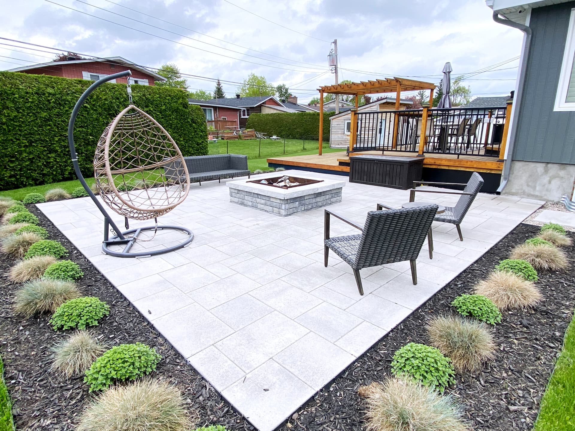 Paver terrace with a stone fire table, planted borders and a cedar deck with pergola behind