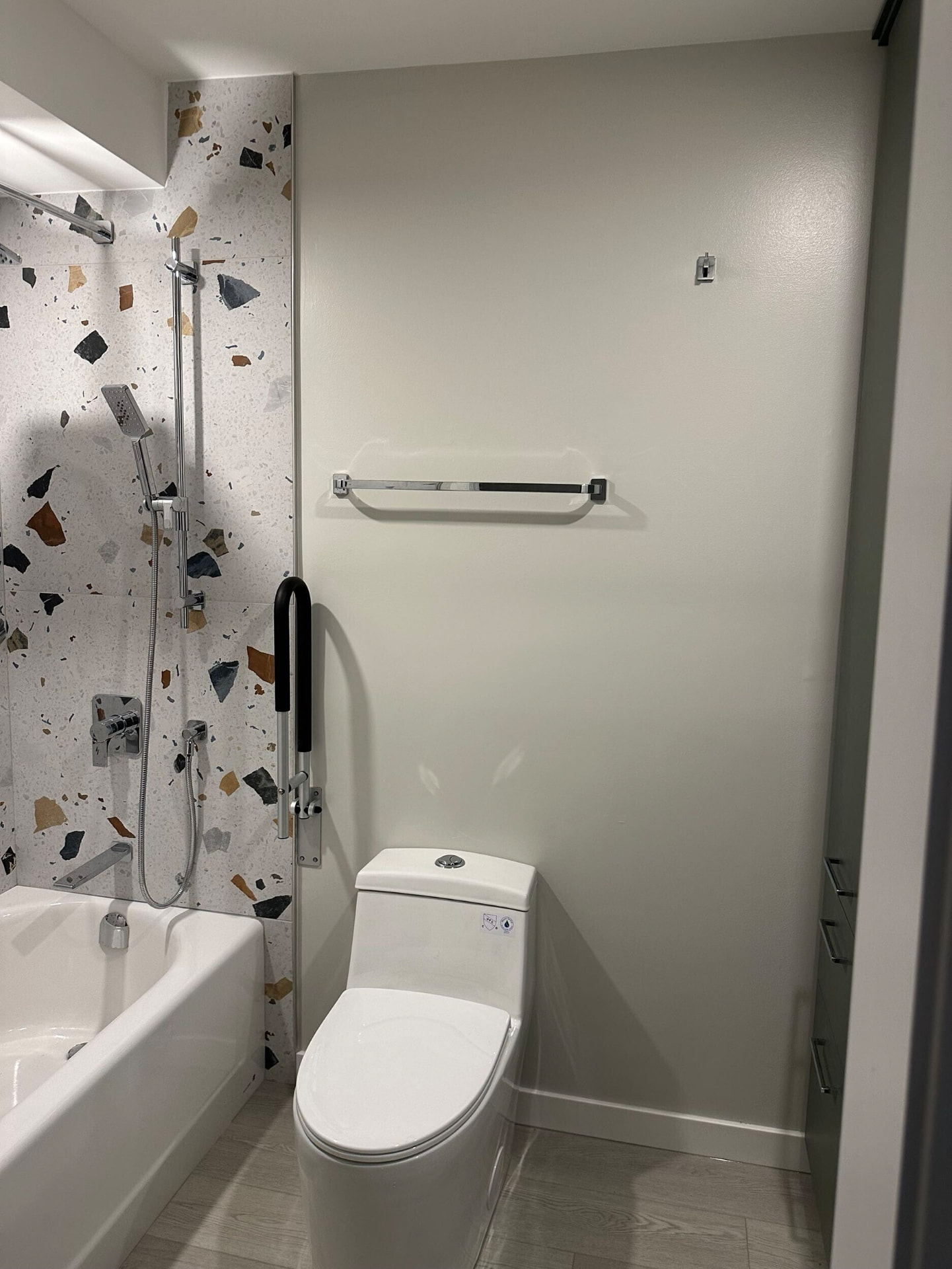 Matte black looped grab bar at the tub entry beside a comfort-height toilet