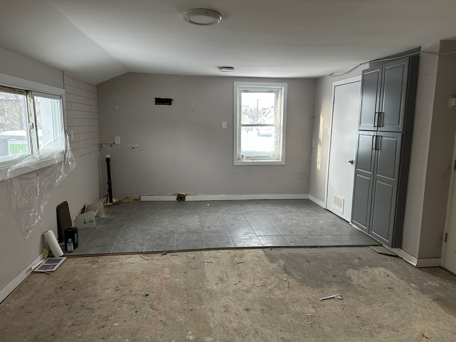 Old kitchen area stripped of cabinets with tile floor and grey pantry unit remaining
