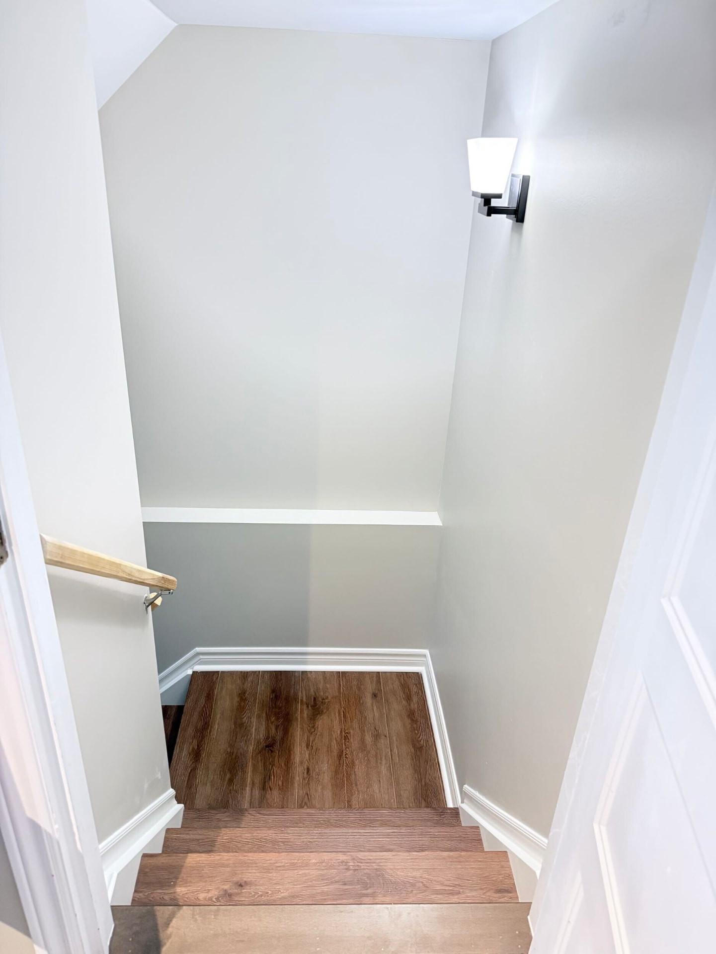 Finished basement stairway with wood-look treads, white trim and a black wall sconce