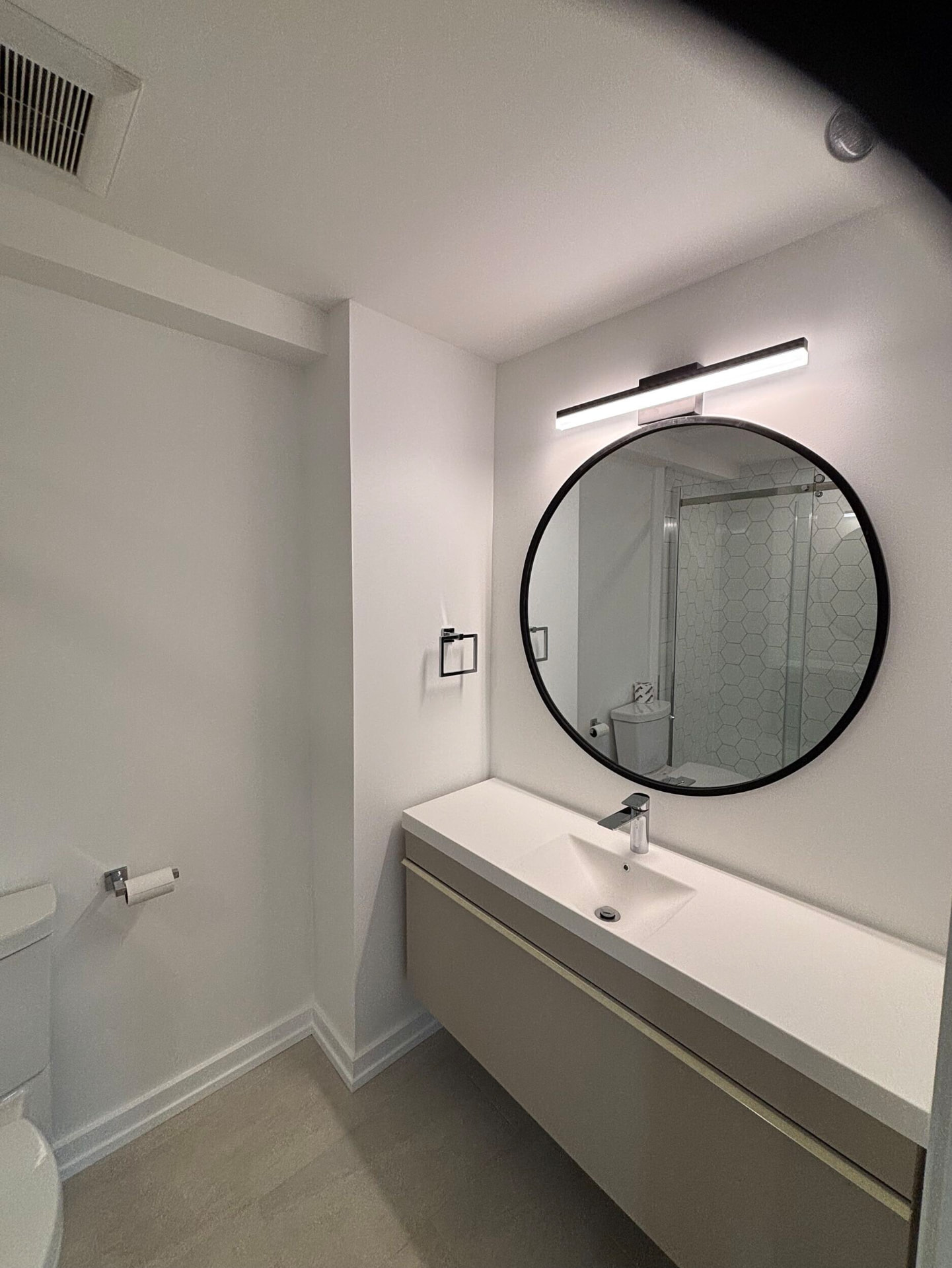 Floating vanity with integrated basin, round black mirror and linear light