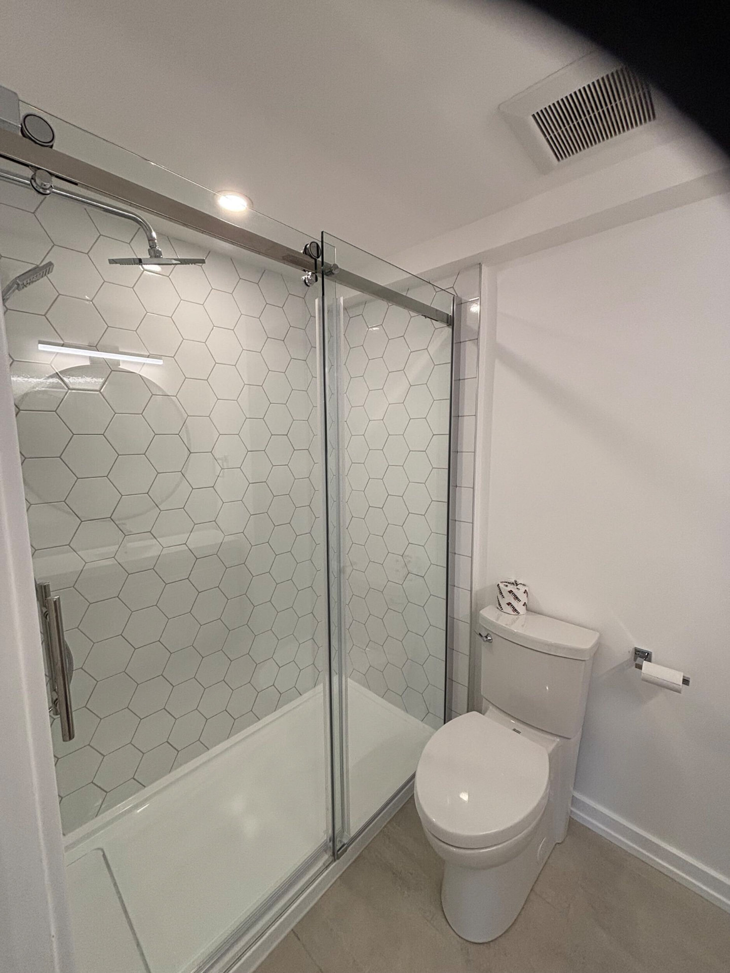 Walk-in shower with white hexagon tile and sliding chrome glass doors beside a toilet