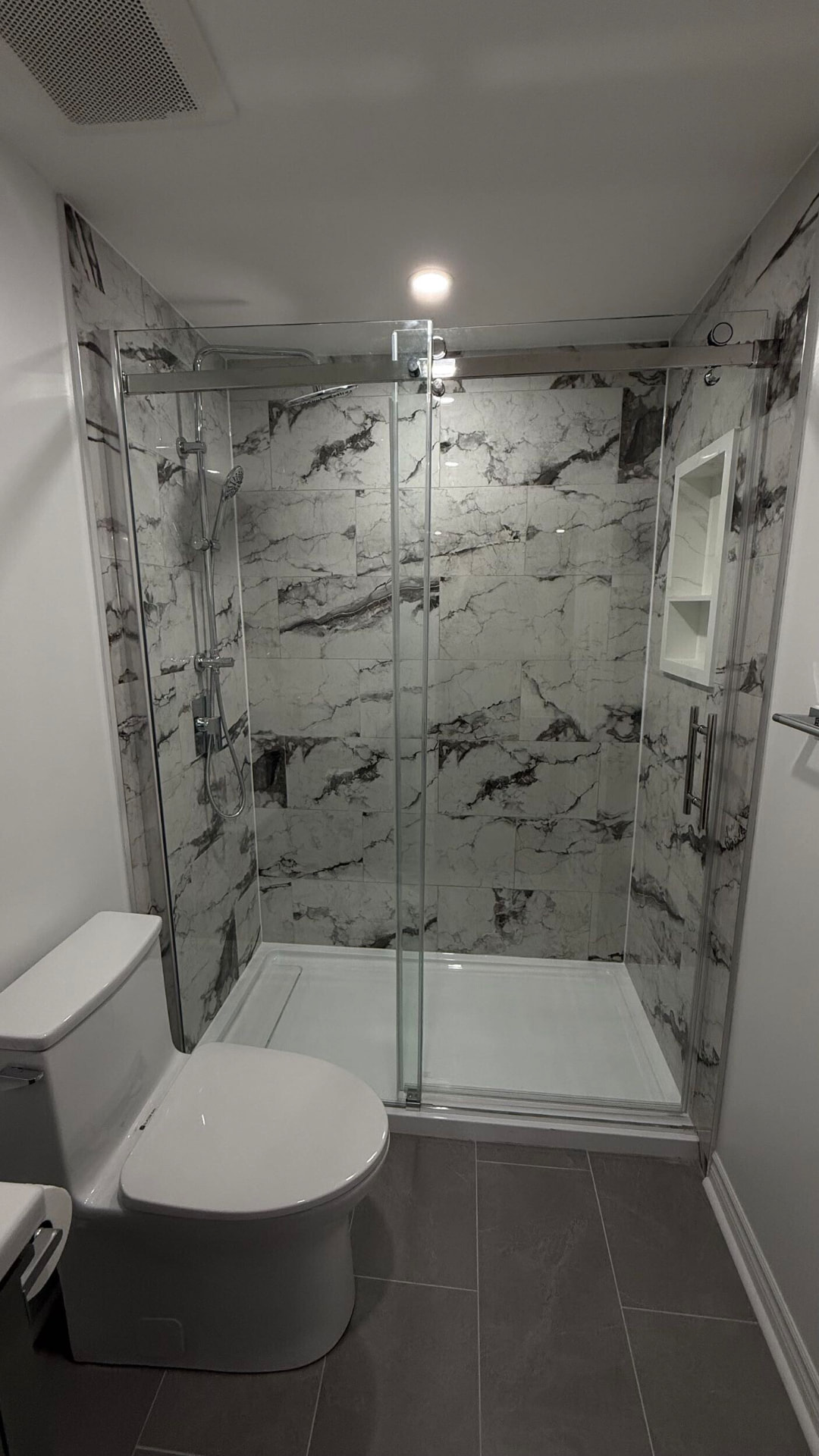 Marble-veined porcelain shower with sliding chrome and glass doors and a low white base