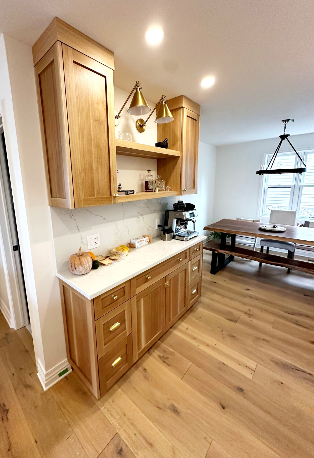 White oak coffee bar with quartz counter, open shelf and brass swing-arm sconces beside the dining table