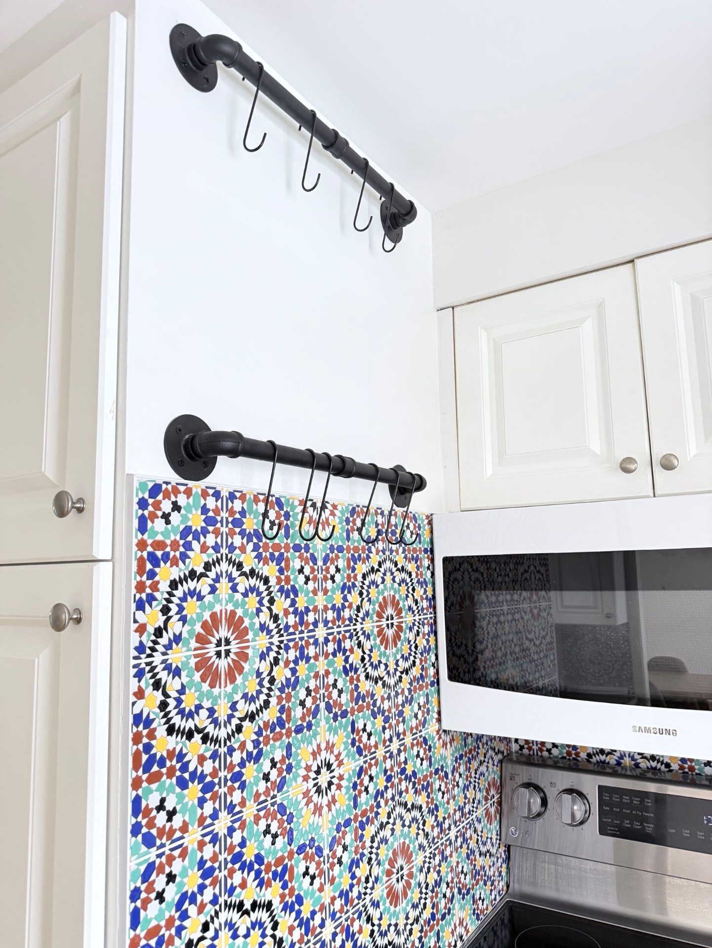 Black cast-iron pot rails with S-hooks mounted above a Moroccan mosaic tile panel