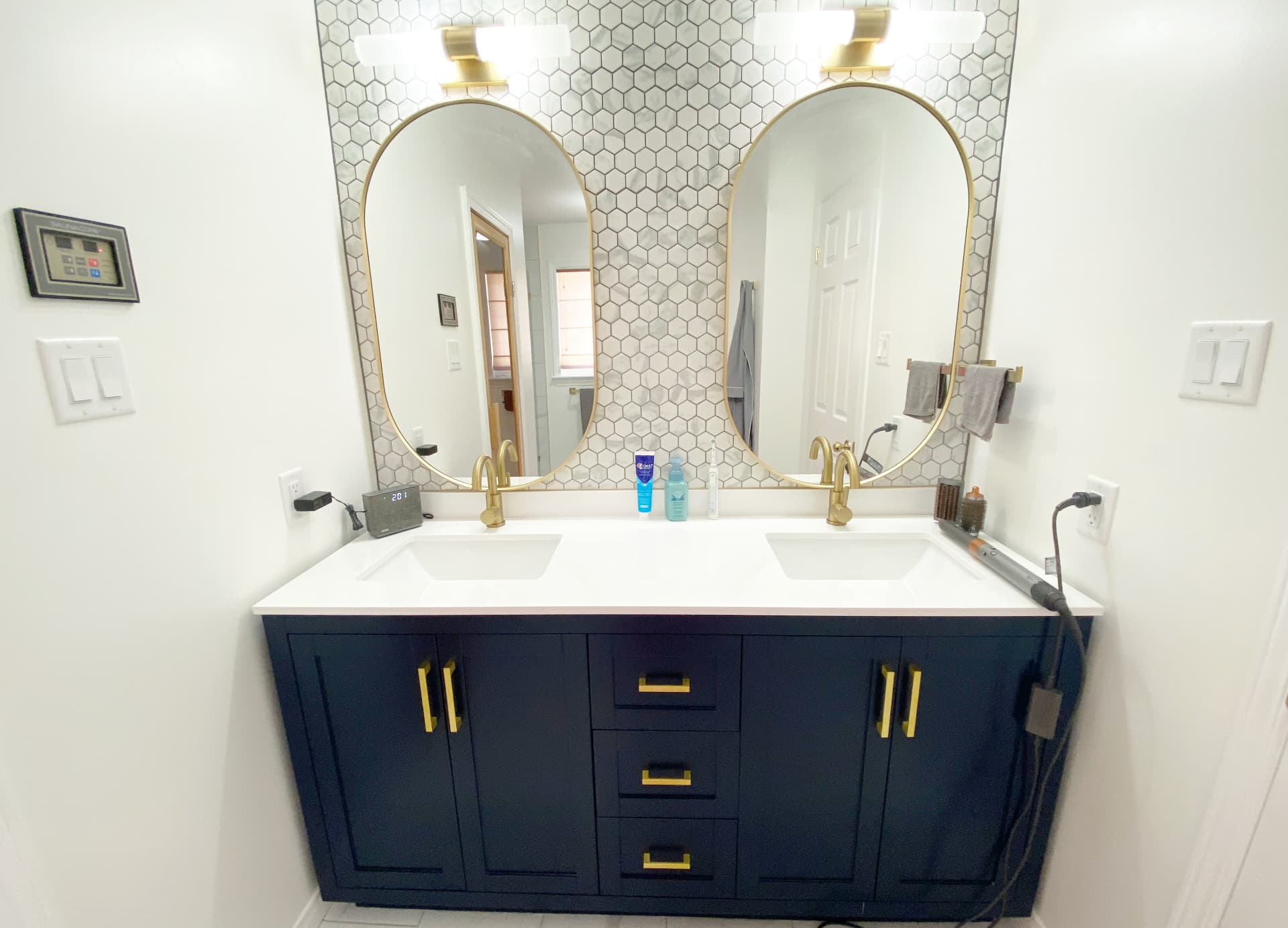 Navy double vanity with quartz counter, arched brass mirrors and hexagon mosaic tile wall