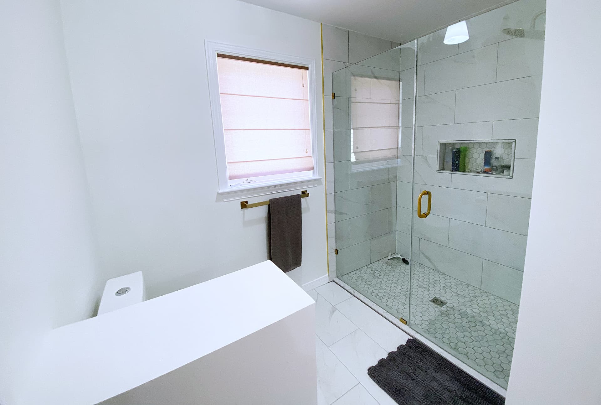 Frameless glass shower with marble-look wall tile, hexagon mosaic floor and a recessed niche