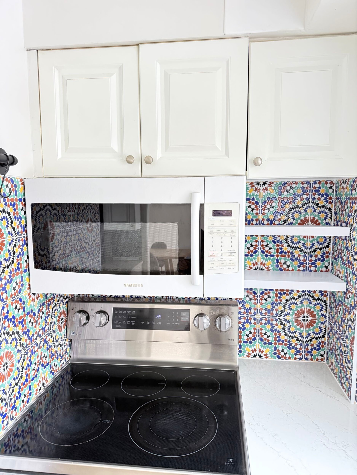 White floating shelves set into a Moroccan tile niche beside a microwave in a galley kitchen