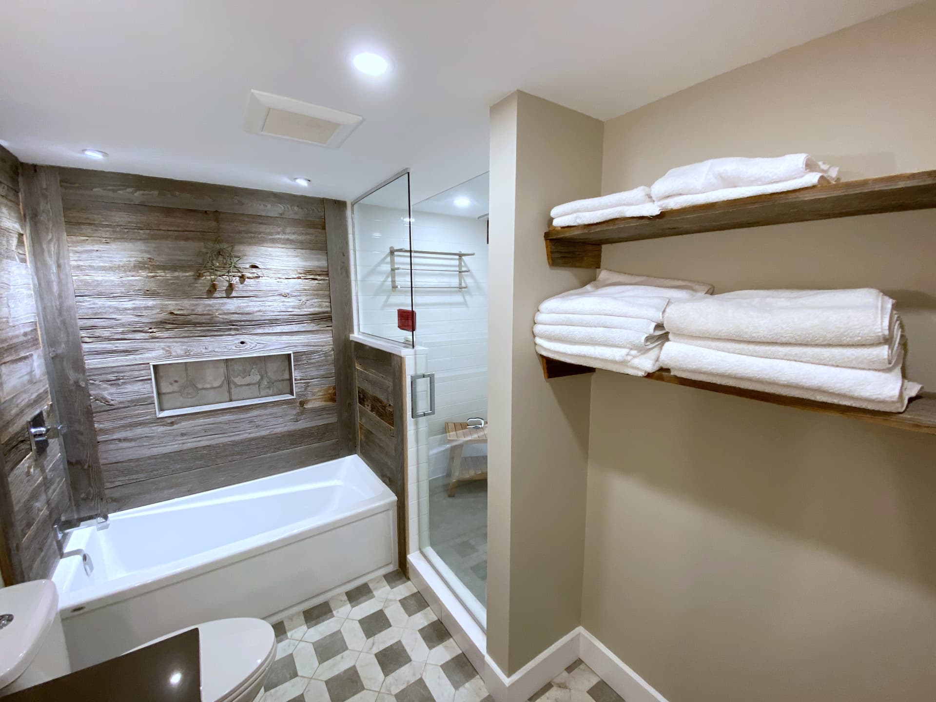 Bathroom with reclaimed barnwood feature wall, white tub, glass shower and hexagon marble floor