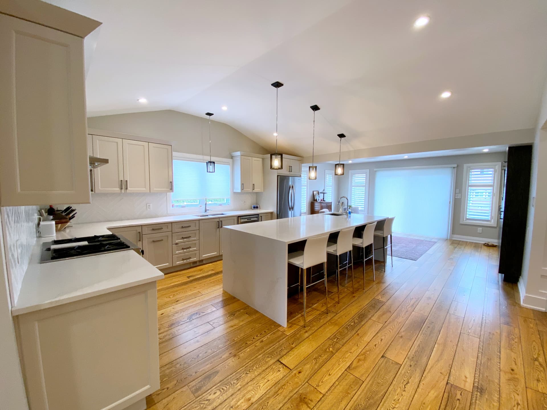 Vaulted kitchen ceiling with three lantern pendants over a long white quartz island