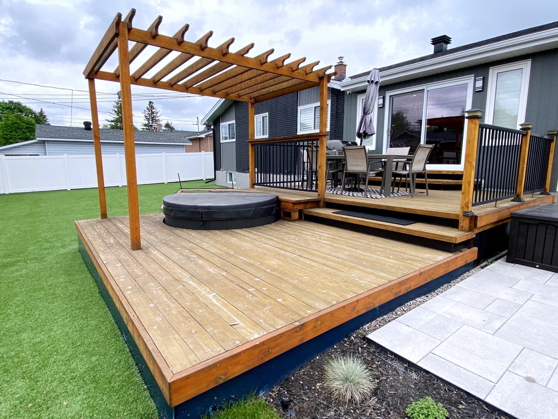 Cedar deck with pergola over a hot tub, black aluminum railing and paver terrace beyond