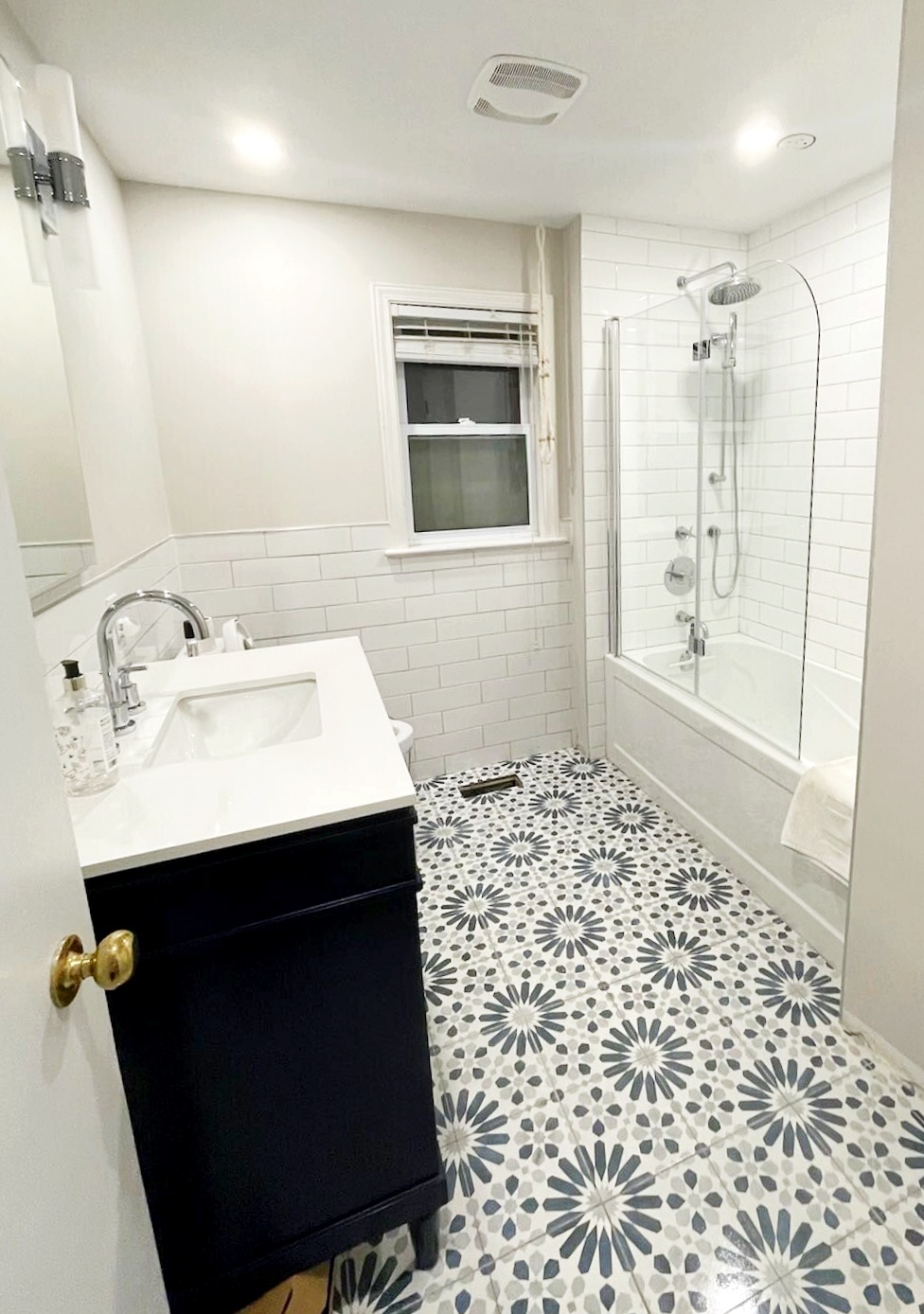 White-tiled Ottawa bathroom with blue-grey patterned floor, navy vanity and glass tub enclosure
