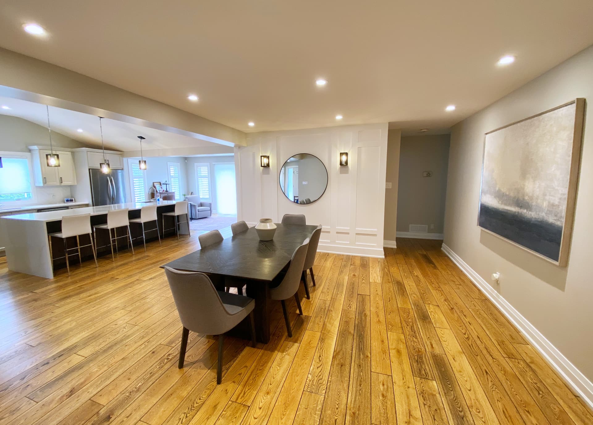 Dining room with a dark timber table, panelled wall, round mirror and paired sconces