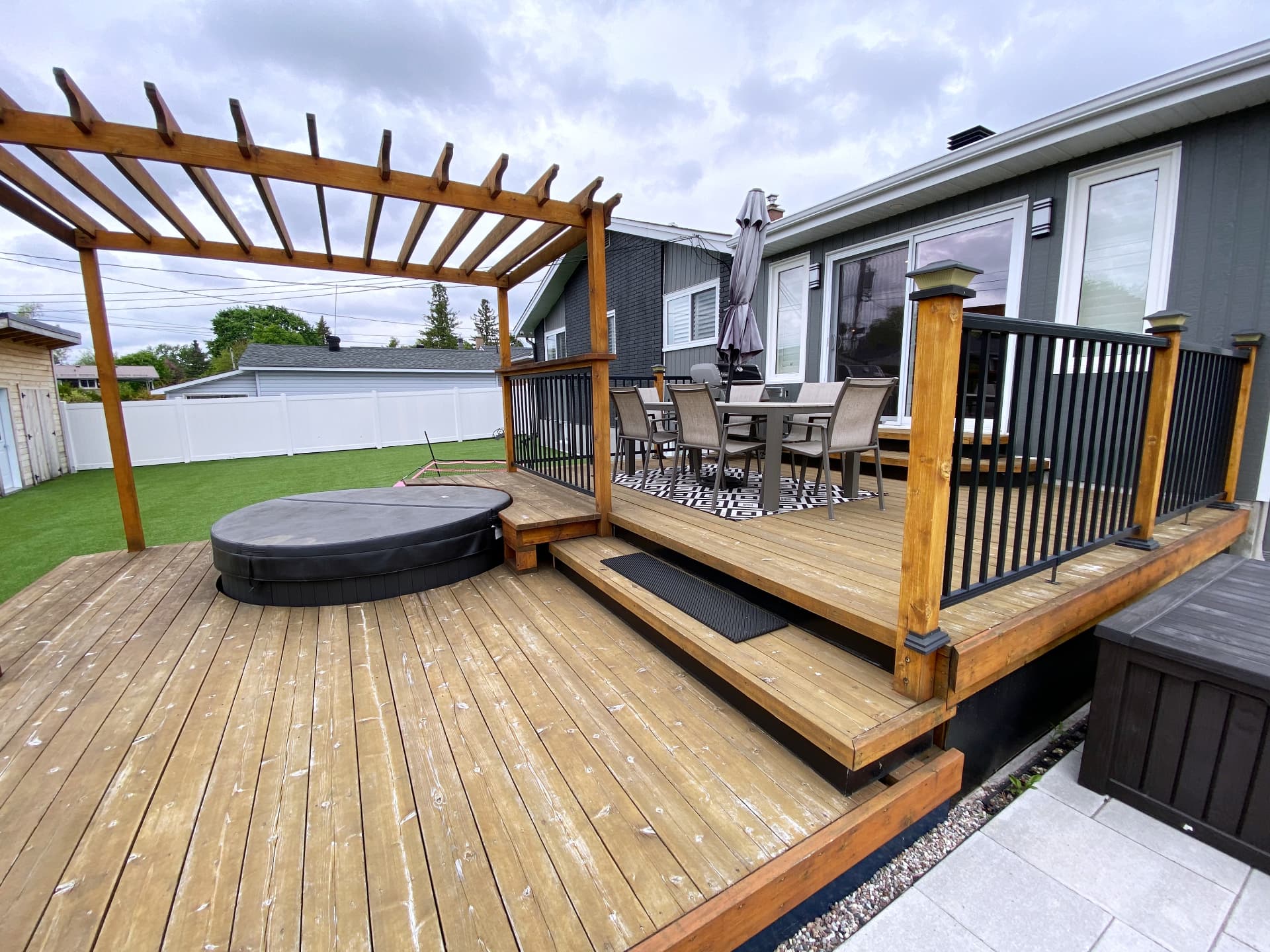 Two-level cedar deck with dining area, pergola and hot tub against dark board and batten siding