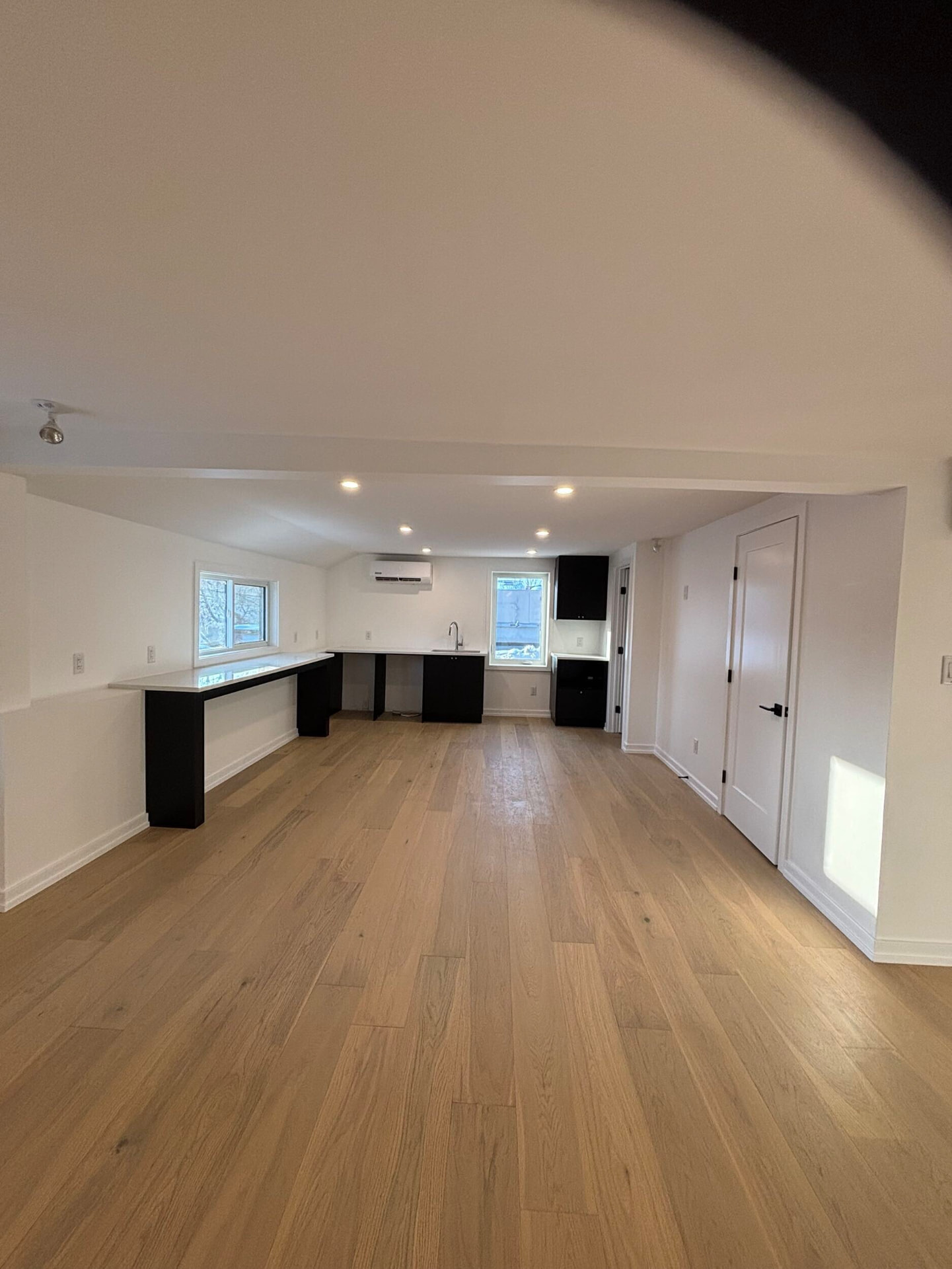 Black kitchenette with quartz counters and a long bar under the windows in an open loft