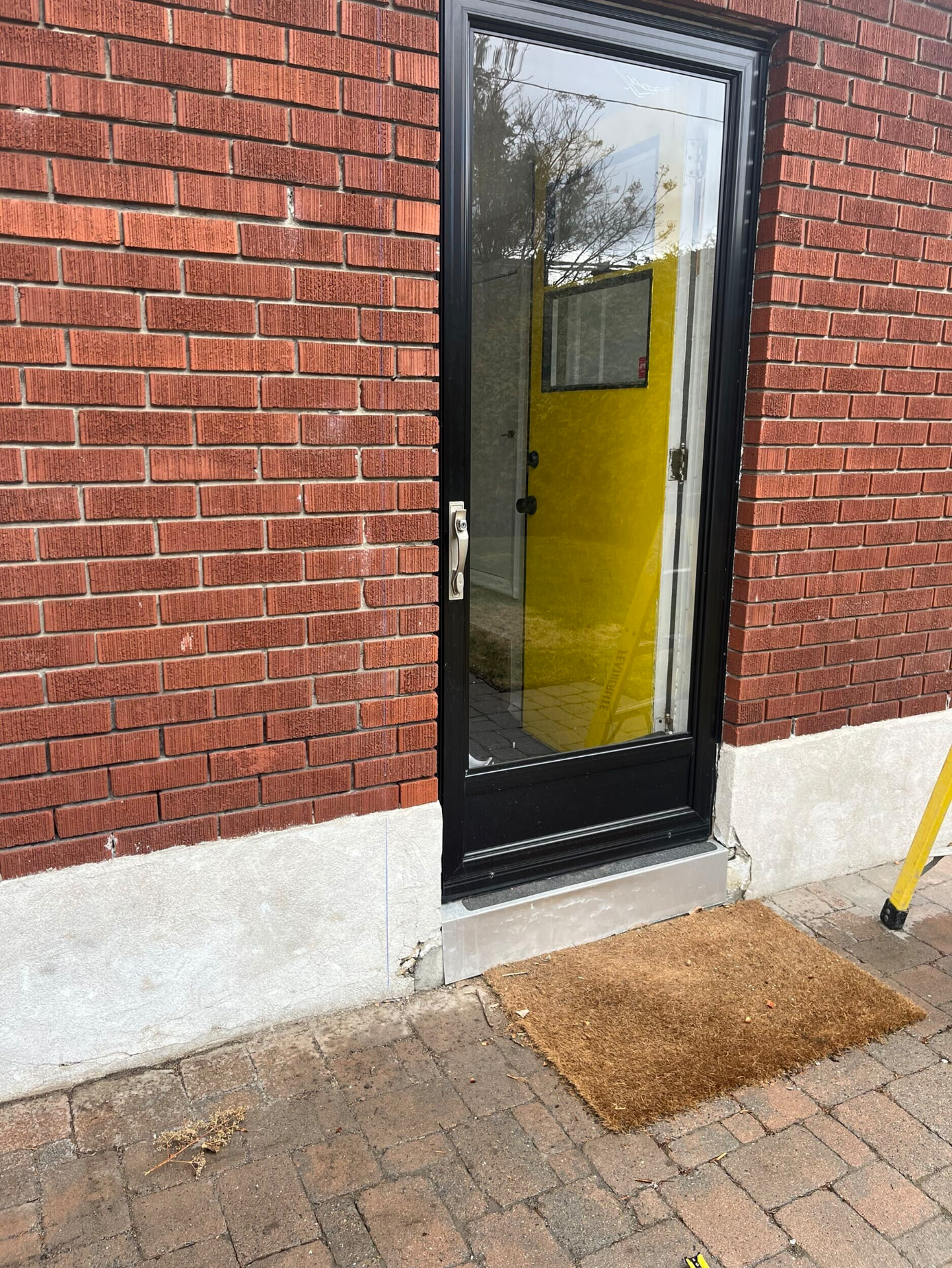 New black-framed full-lite entry door set cleanly into red brick with a poured concrete sill
