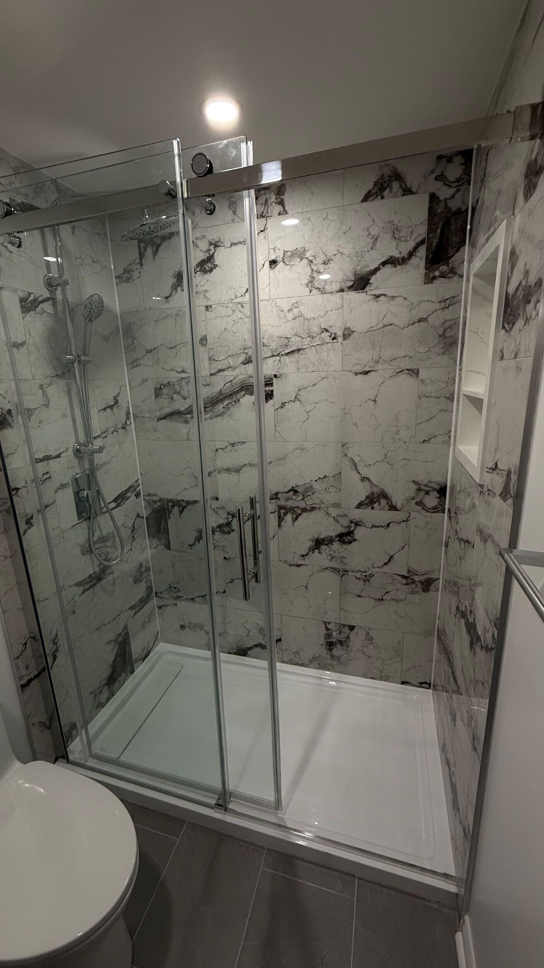 Marble-veined porcelain shower walls behind chrome-framed sliding glass doors