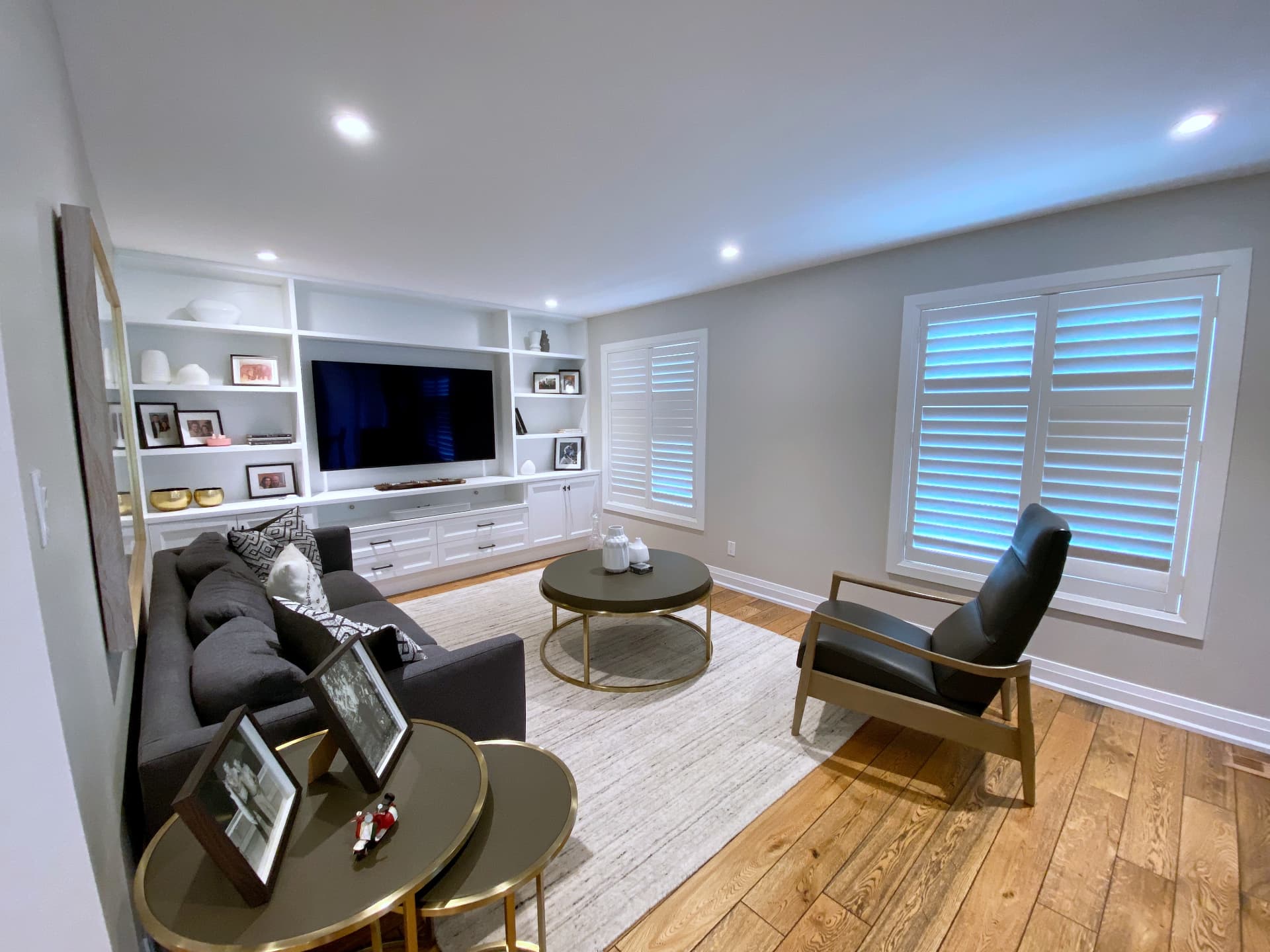 Family room with plantation shutters, oak plank flooring and white built-in cabinetry