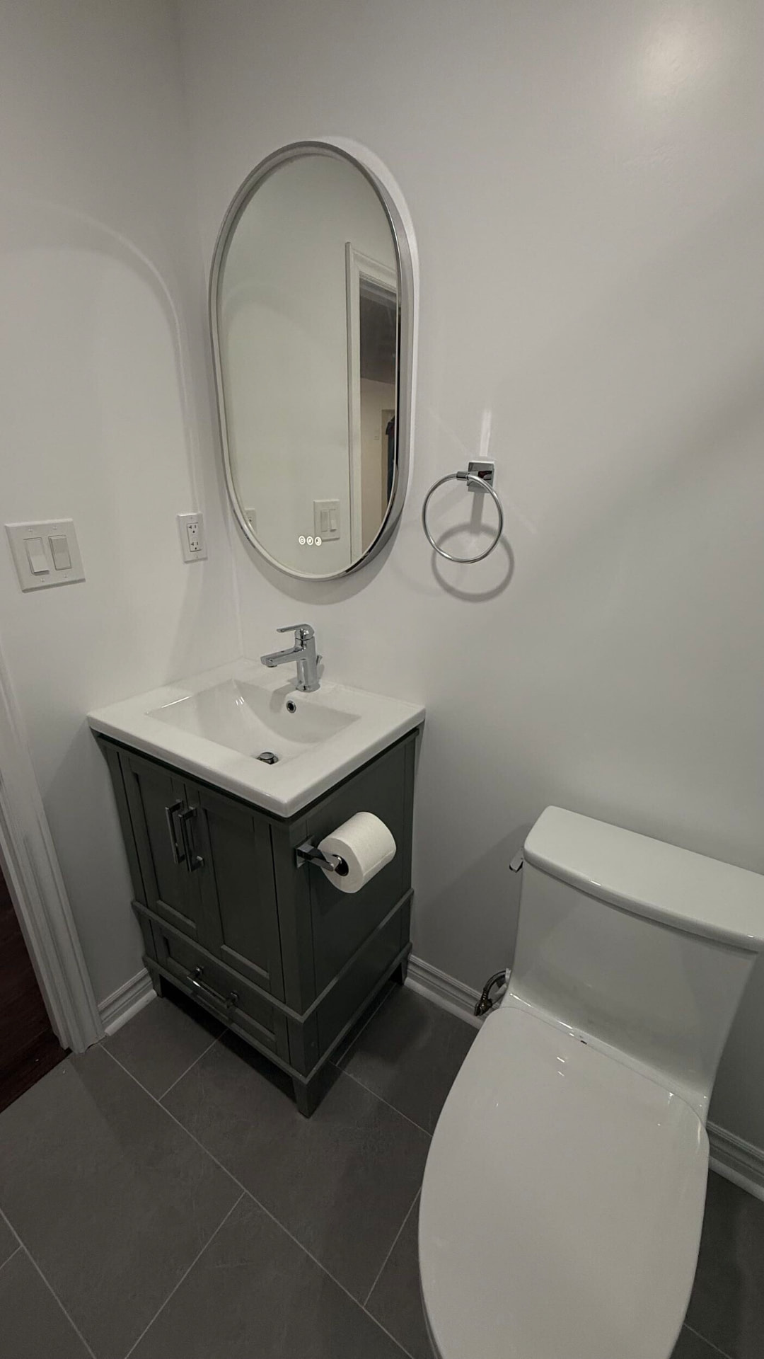 Small powder room with a dark green vanity, oval framed mirror and grey floor tile