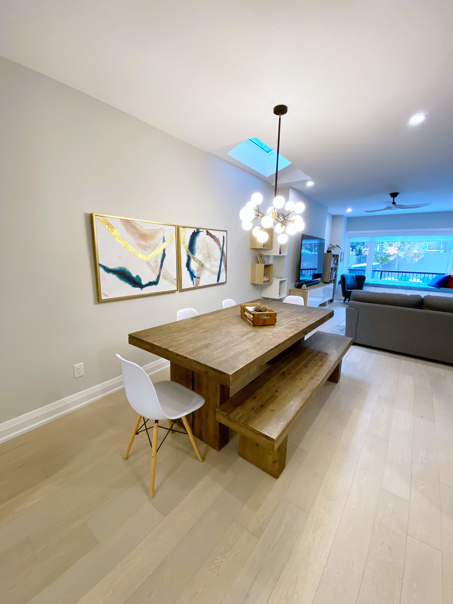 Skylit dining room with a globe chandelier, timber table and view through to the living room