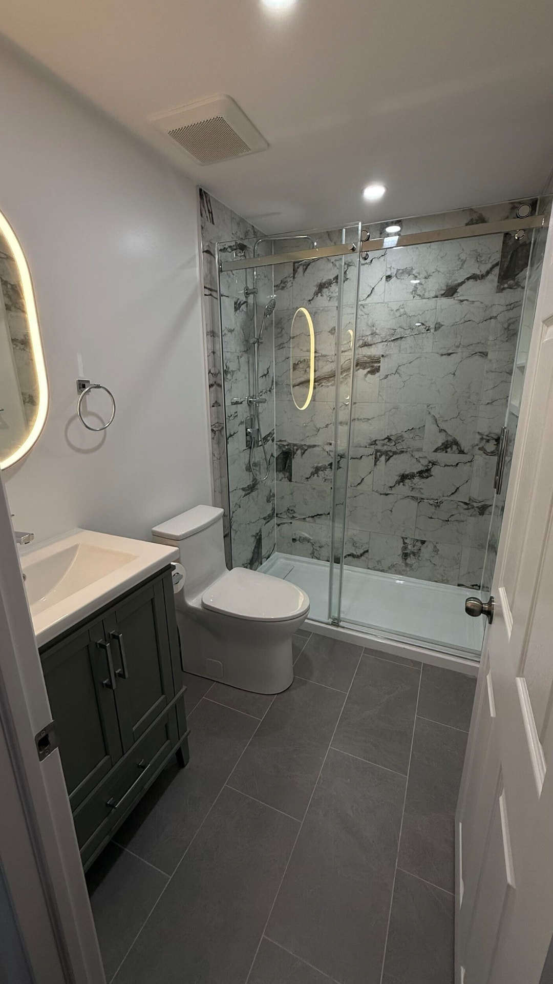 Wide view of the lower-level bathroom from the doorway showing vanity, toilet and glass shower