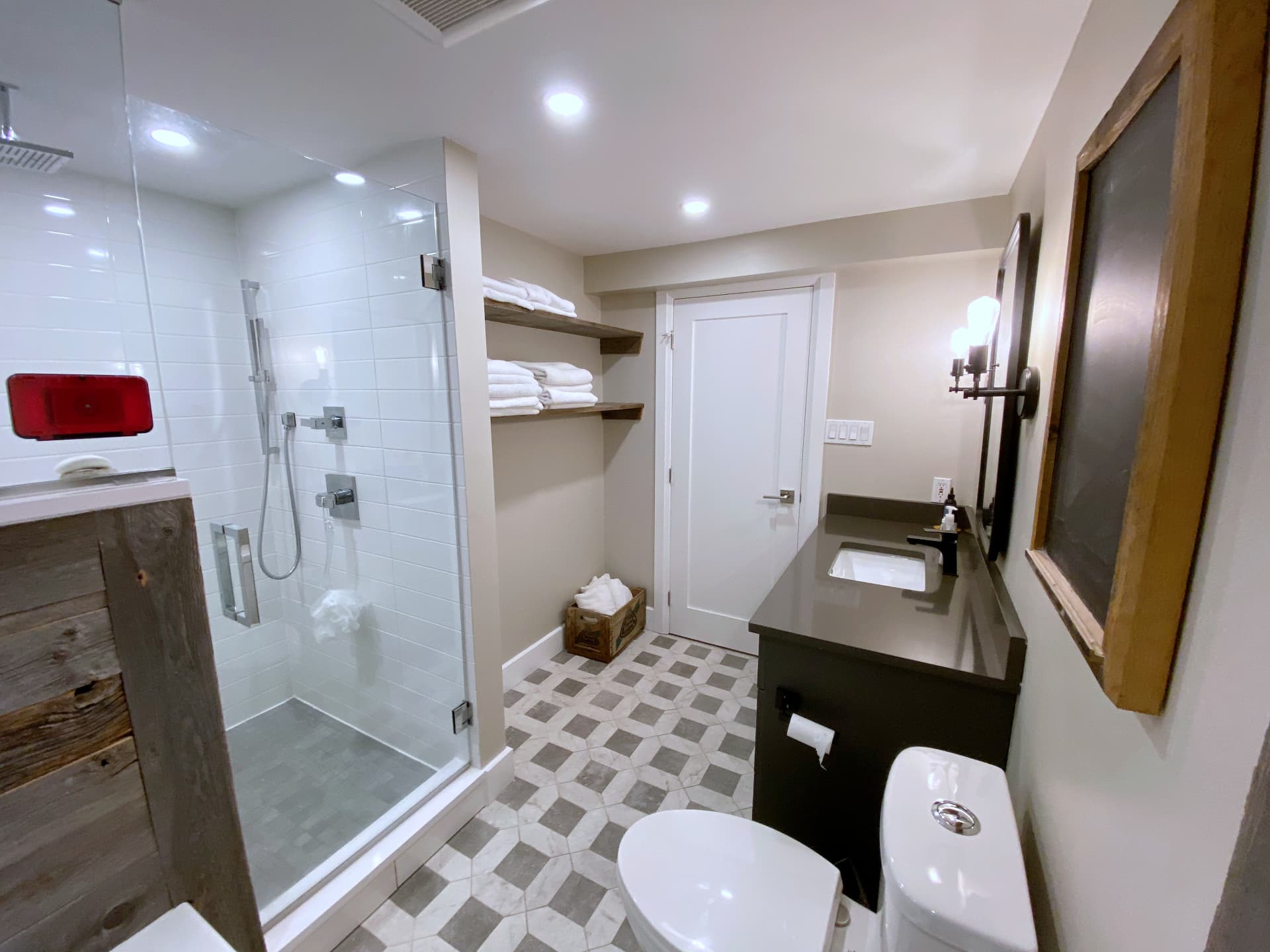 Bathroom looking toward reclaimed wood floating shelves and a glass shower enclosure