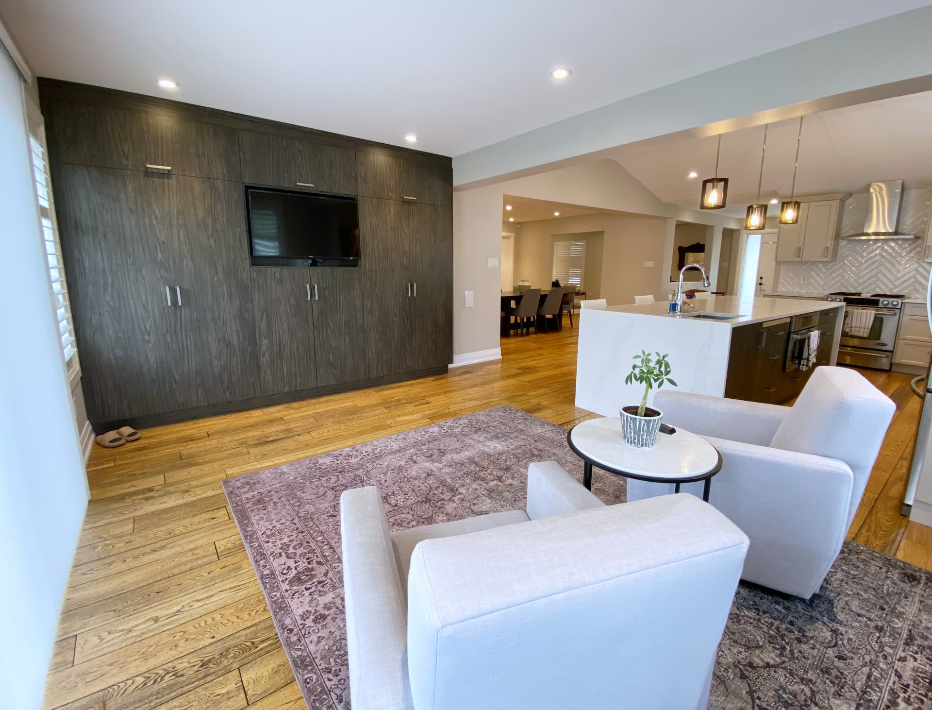 Full-height grey oak storage wall with recessed television beside an open kitchen and island