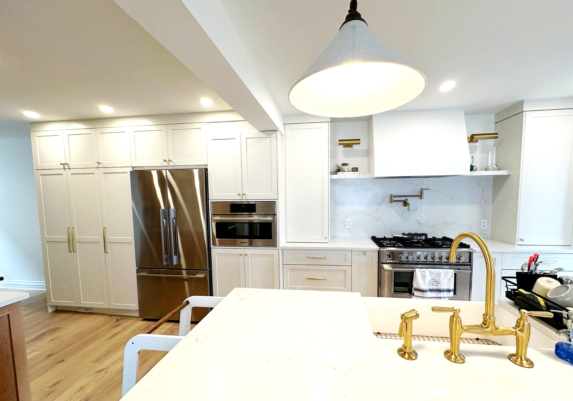 Wide view of the finished kitchen with cream cabinetry, brass fixtures and a quartz island
